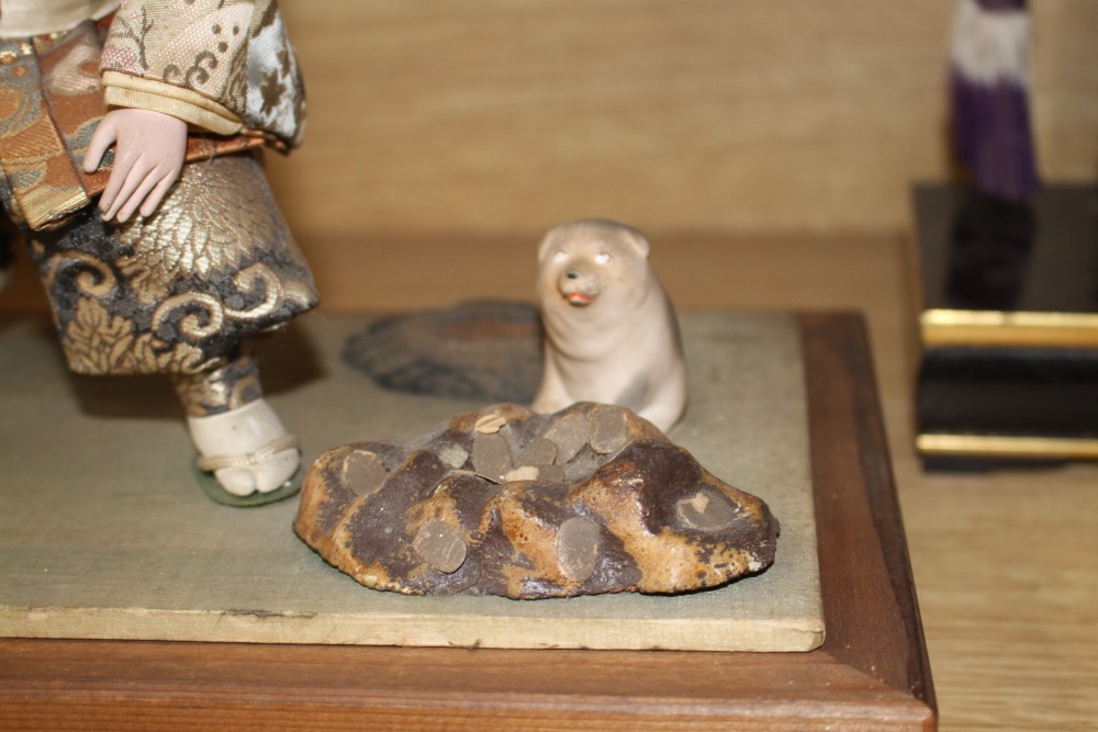 A Japanese late Meiji period composition and fabric figure of a boy farmer holding an adze with puppy seated nearby, mounted on display